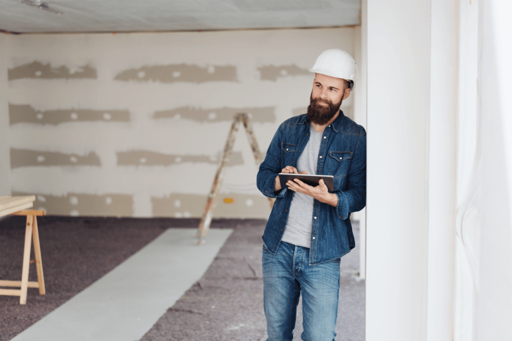 Homme souriant portant une chemise en jean et un casque de construction avec une tablette à la main